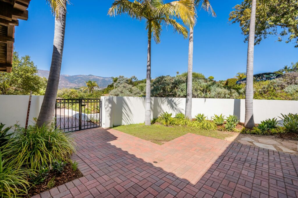 the brick patio of a house has many trees and a fence